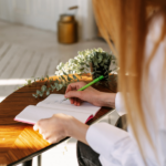 Image: A woman hands, holding a pen and a blank journal, poised to start writing. Image represents choosing journaling instead of just searching Am I An Alcoholic on the internet.