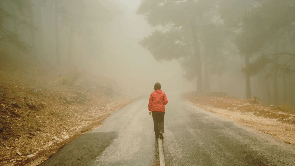 Woman walking alone in the fog on a tree-lined road, contemplating the shame of drinking too much.