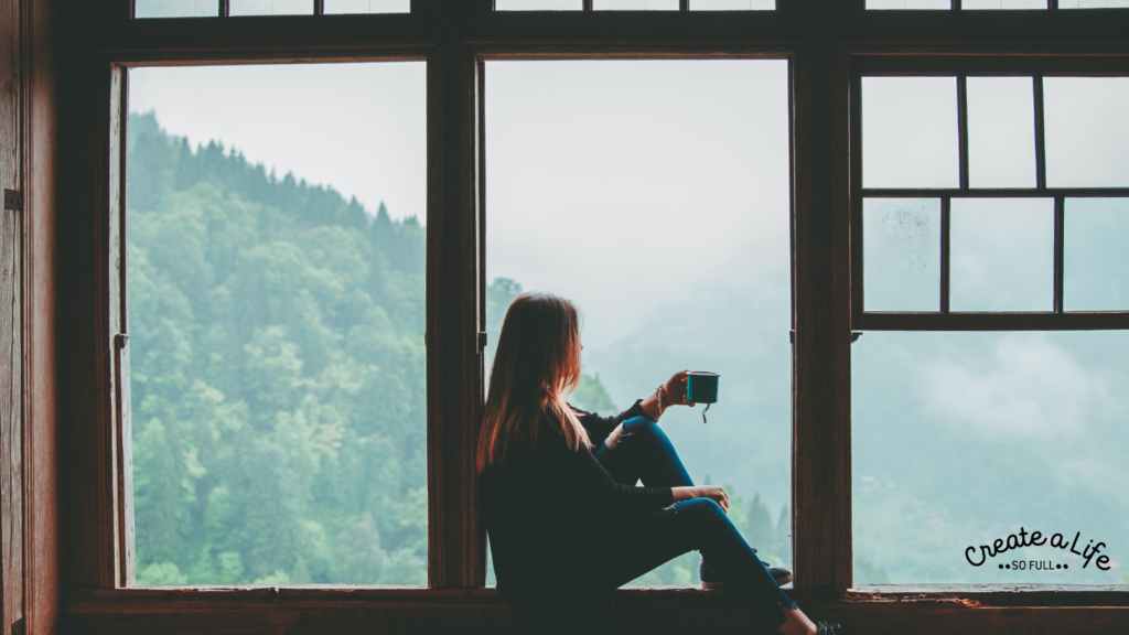 Woman sitting on the edge of a window, holding a mug and looking out, wondering how to make sobriety last for the long term