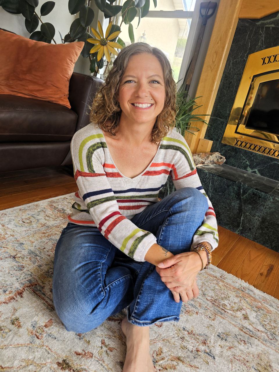 Image: Julie Miller, RCP Alcohol Free Coach sitting on a rug, legs crossed, in front of a fireplace.