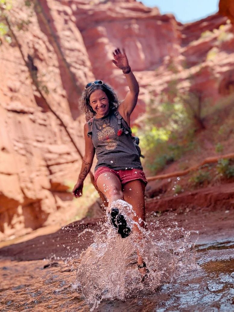 Julie Miller, Sober Coach kicking up water in a red Utah canyon.